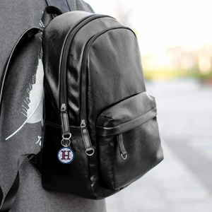 Black backpack with an acrylic keychain with a maroon letter H
 on a blurred background