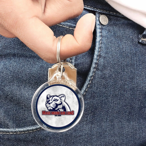 acrylic keychain with a Maus Mountain lions logo held by a finger against denim fabric