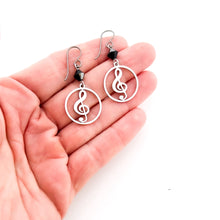 close up of hand holding stainless steel treble clef hoop charm earrings with black Swarovski crystal earrings