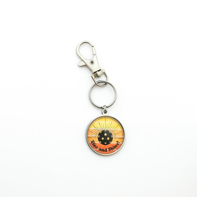 stainless steel pickleball keychain with yellow and orange Rise and Shine graphic