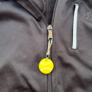 ceramic tennis ball zipper pull hanging from a black jacket