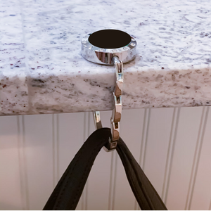 silver purse hook with black center hanging from a granite counter top