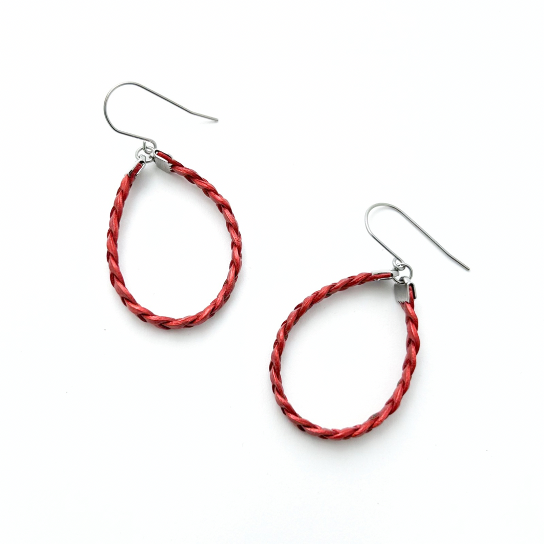 A pair of red braided leather hoop earrings with silver stainless steel accents on a white background.