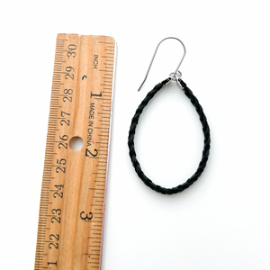 a single black braided leather hoop earring with titanium ear wires measured next to a ruler