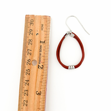 wooden ruler next to a single reddish brown leather hoop earring with stainless steel accents and titanium ear wires