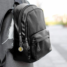 black leather backpack with a personalized acrylic round keychain with a yellow initial B on black pattern background