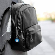 Black leather backpack with a custom acrylic keychain with a jersey number 25 and personalized text option outdoors